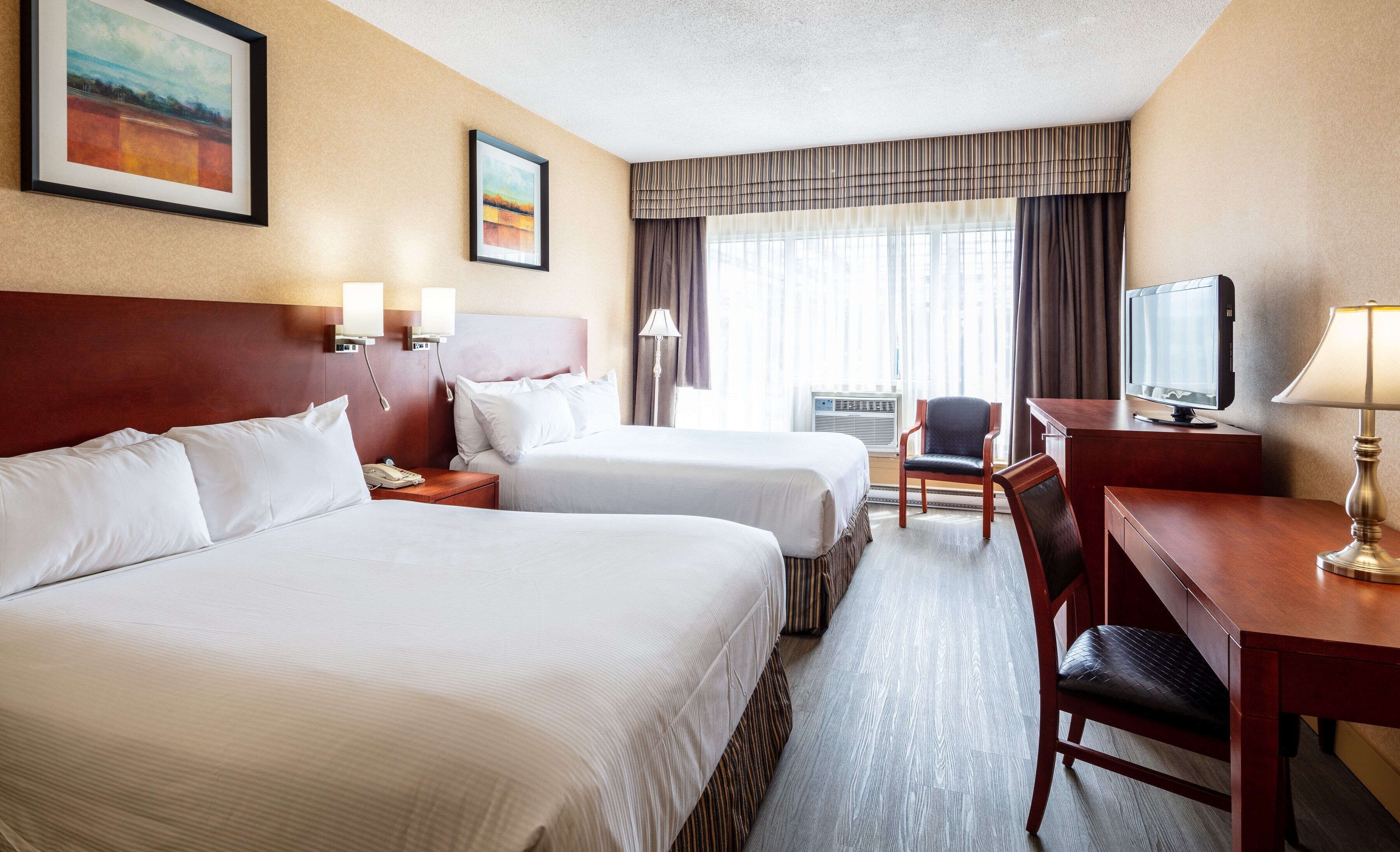 Quarto de hotel com duas camas, uma escrivaninha, uma cadeira, uma televisão e um quadro na parede.