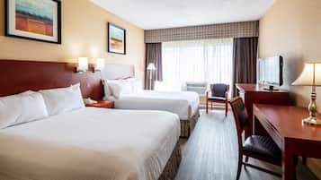Quarto de hotel com duas camas, uma escrivaninha, uma cadeira, uma televisão e um quadro na parede.