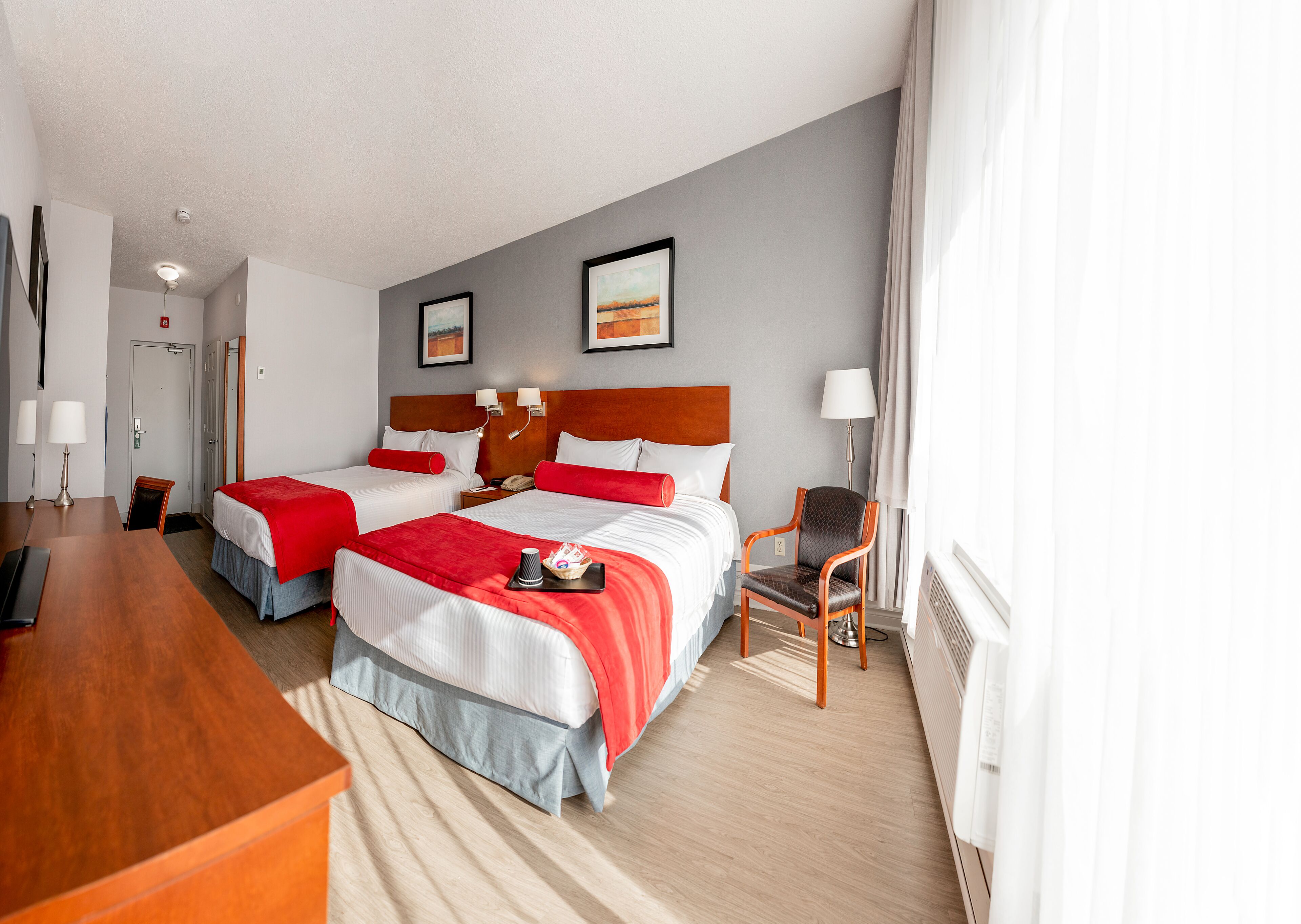 A hotel room with two beds, a desk, a chair, and a lamp.