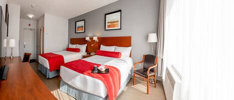 A hotel room with two beds, a desk, a chair, and a lamp.