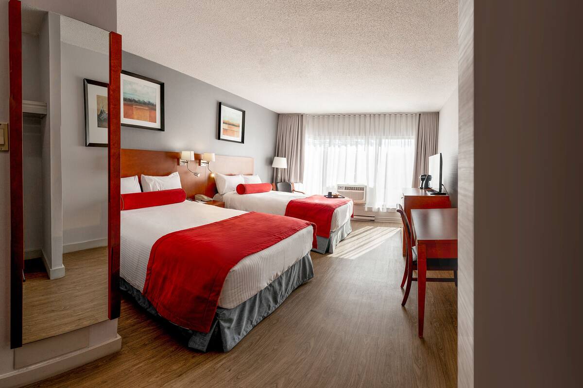 A hotel room with two beds, a desk, and a chair.