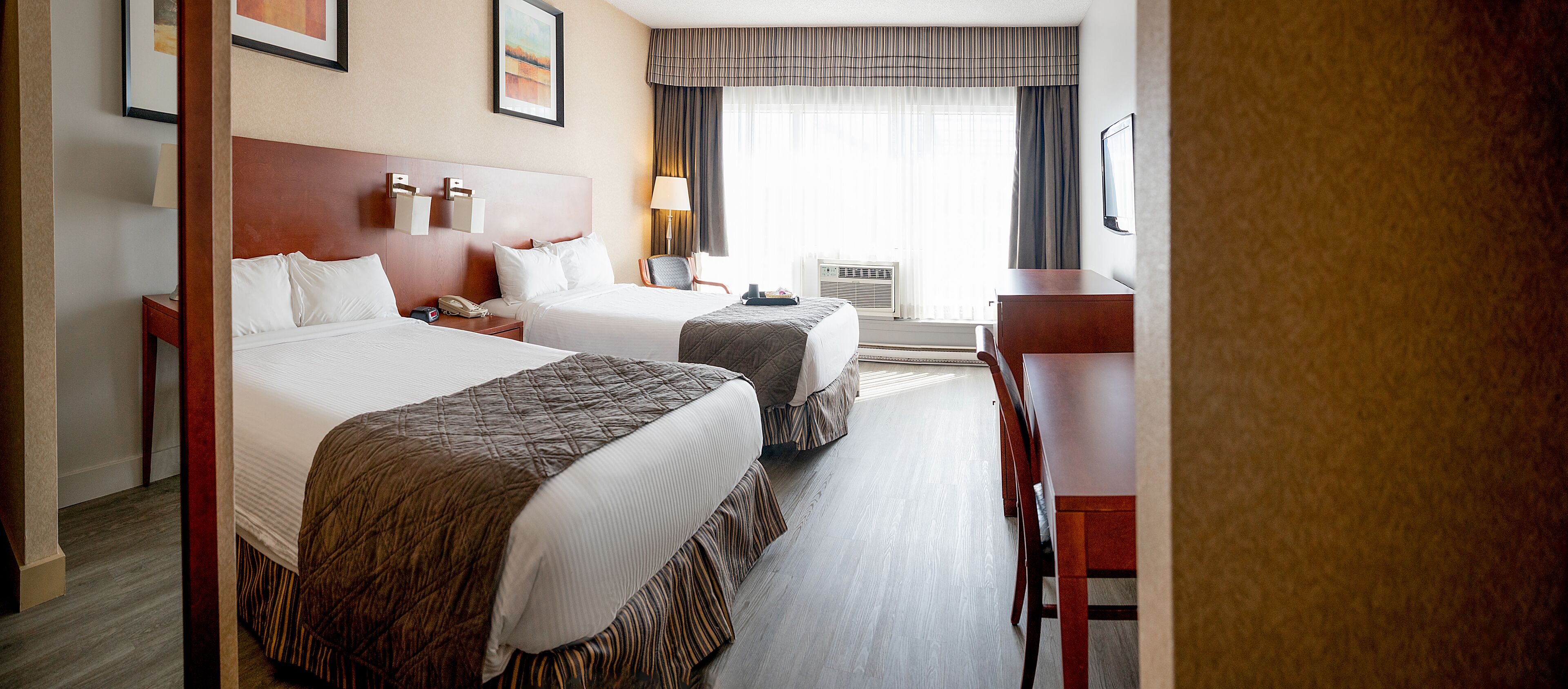 Ein Hotelzimmer mit zwei Betten, einem Schreibtisch, einem Sessel, einem Telefon und einer Klimaanlage.
