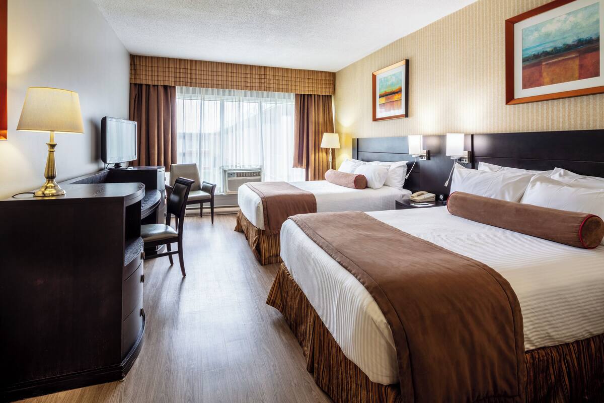 A hotel room with two beds, a desk, a chair, a television, and a painting on the wall.