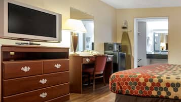 Habitación de hotel con televisor, escritorio, silla, microondas y cama con cubrecama estampado.