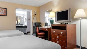 Habitación de hotel con dos camas, un escritorio con silla, televisor, lámpara, microondas y cómoda.