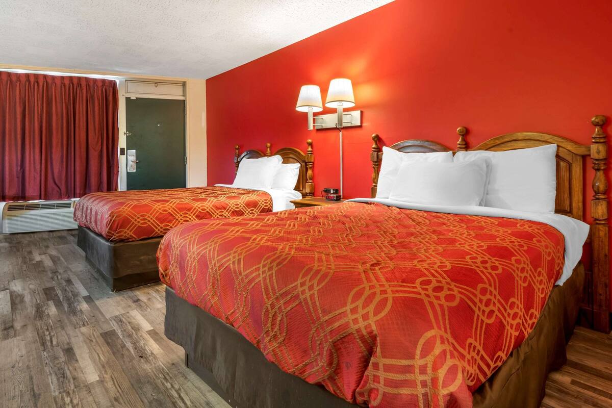 Une chambre d’hôtel avec deux lits, des murs rouges, des têtes de lit en bois et une couvre-lit rouge à motifs.