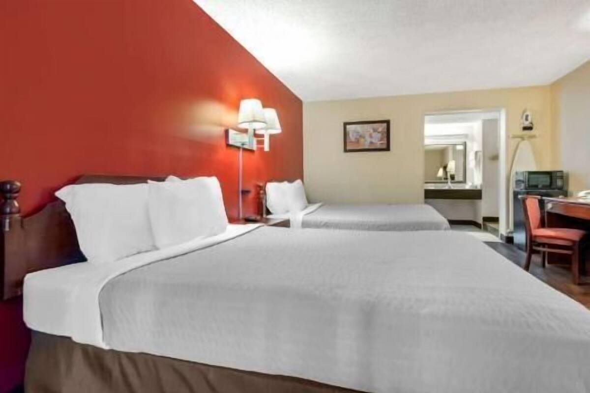 Une chambre d’hôtel avec deux lits, un bureau, une chaise, une lampe et un miroir.