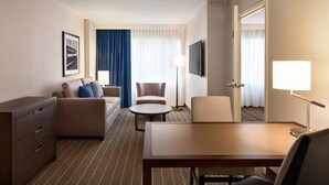 A hotel room with a sofa, two armchairs, a small table, a TV, and a dresser. - Embassy Suites Boston Logan Airport (Boston)