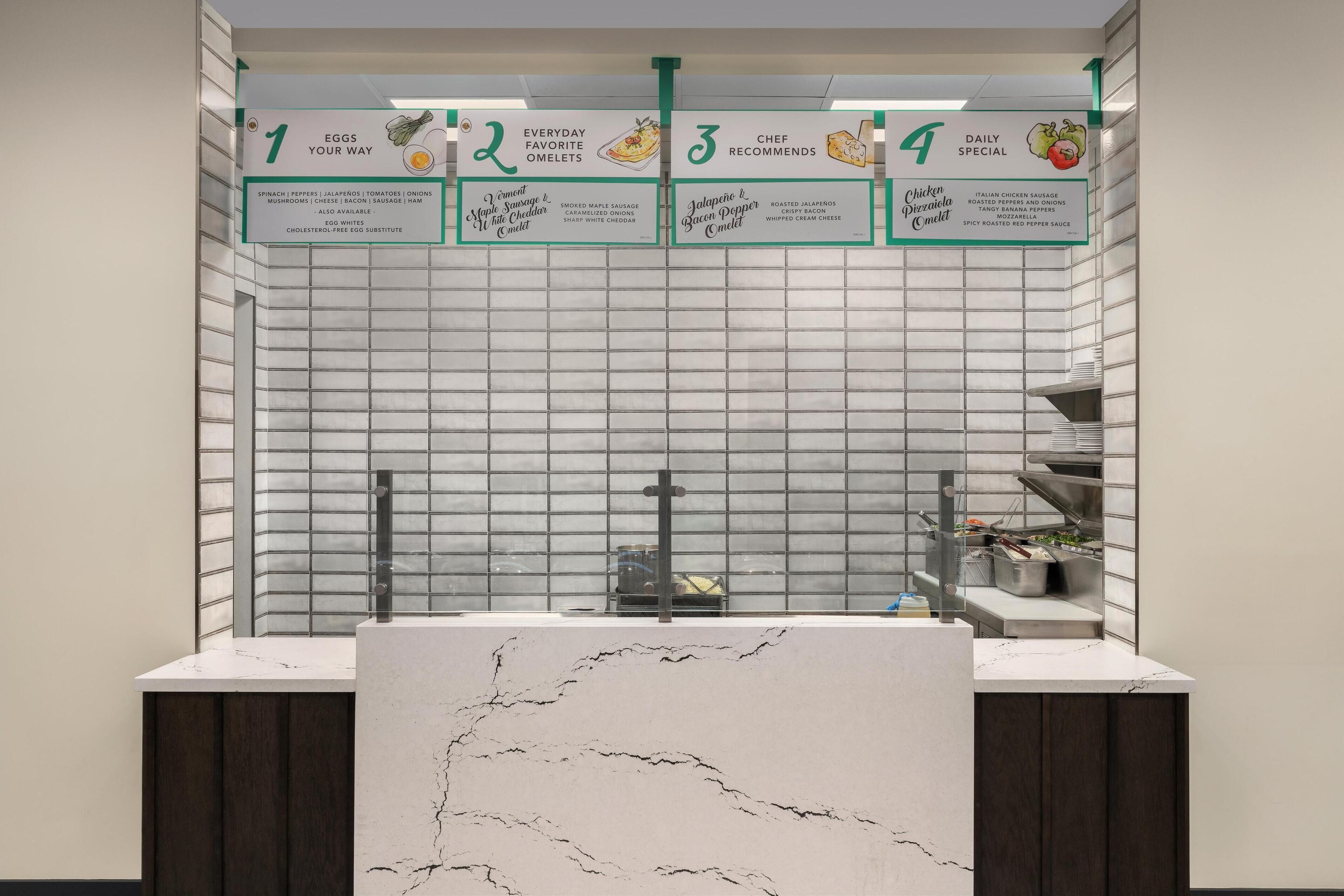 Un comptoir de restaurant avec un dessus en marbre et un tableau affichant le menu, divisé en quatre sections : 1) Œufs préparés à votre goût, 2) Omelettes, les classiques du jour, 3) Suggestions du chef, et 4) Plat du jour.