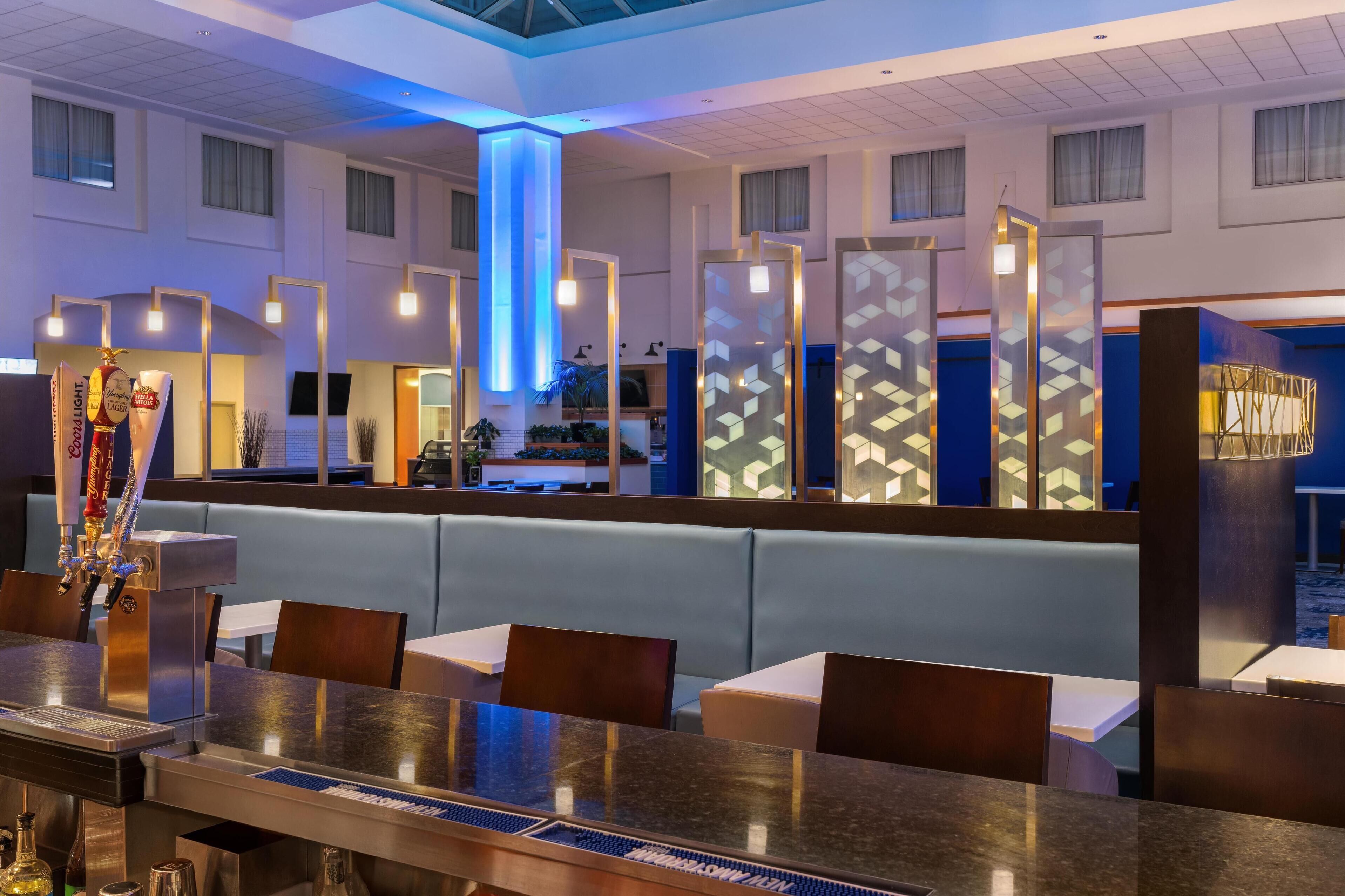 Un moderno vestíbulo de hotel con zona de bar, asientos e iluminación decorativa.