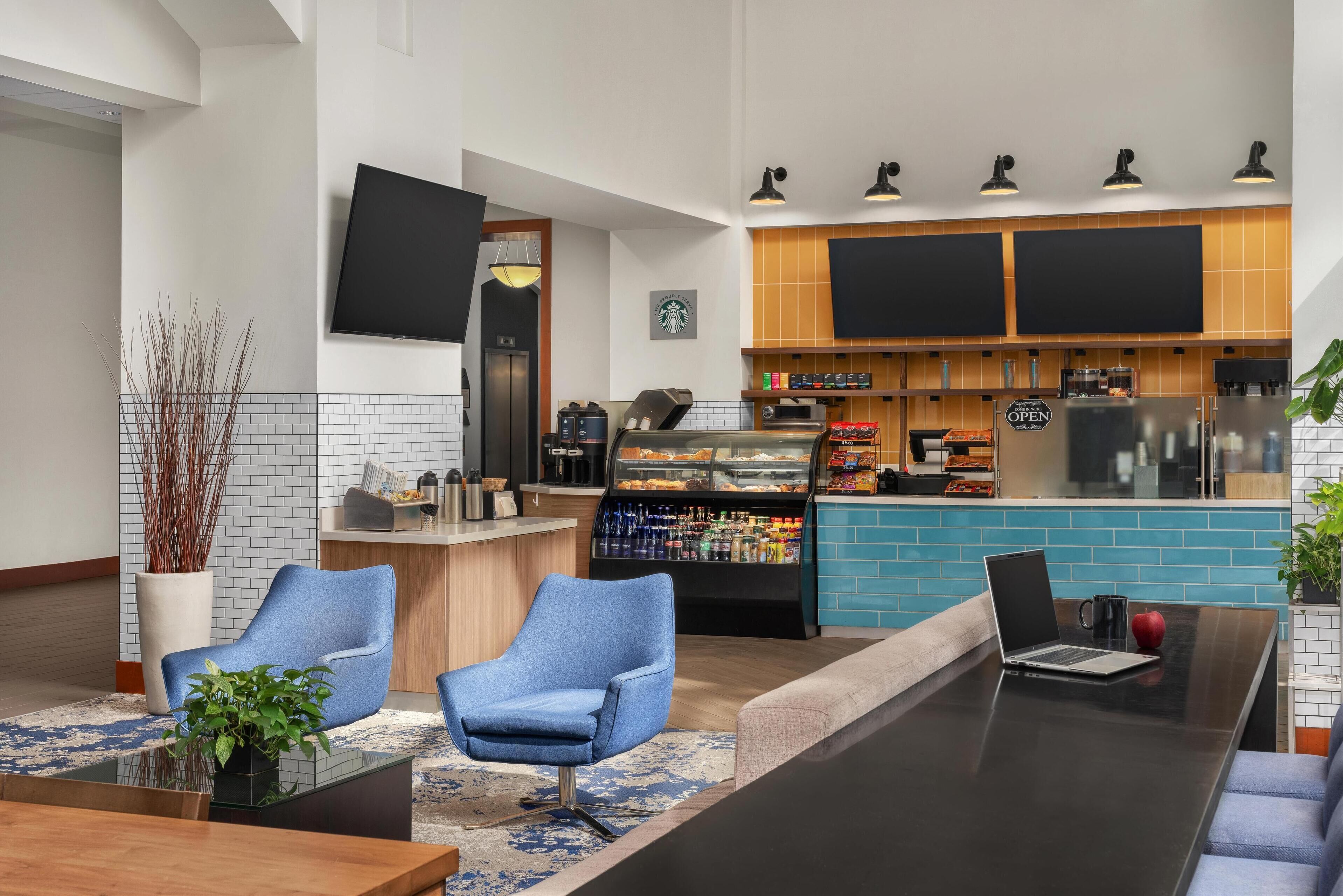 Un hall d’hôtel moderne doté d’espaces de détente, d’un bar à café et d’un téléviseur à écran plat.