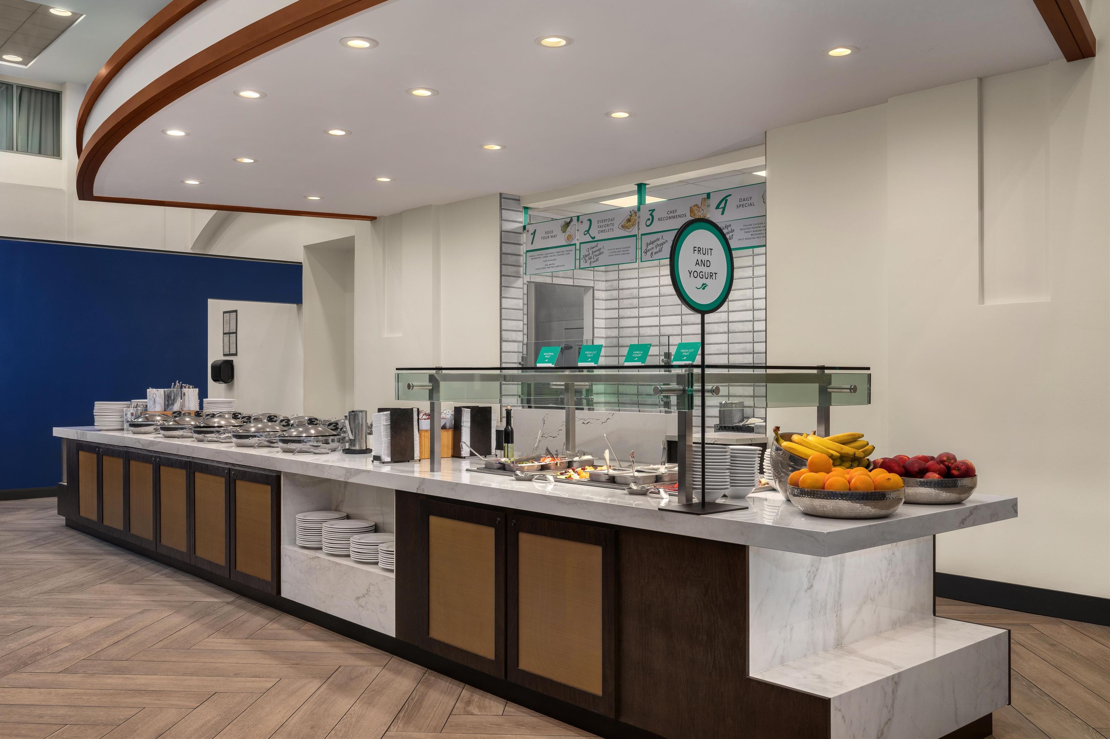 A buffet setup with various food items and a sign indicating fruit and yogurt.