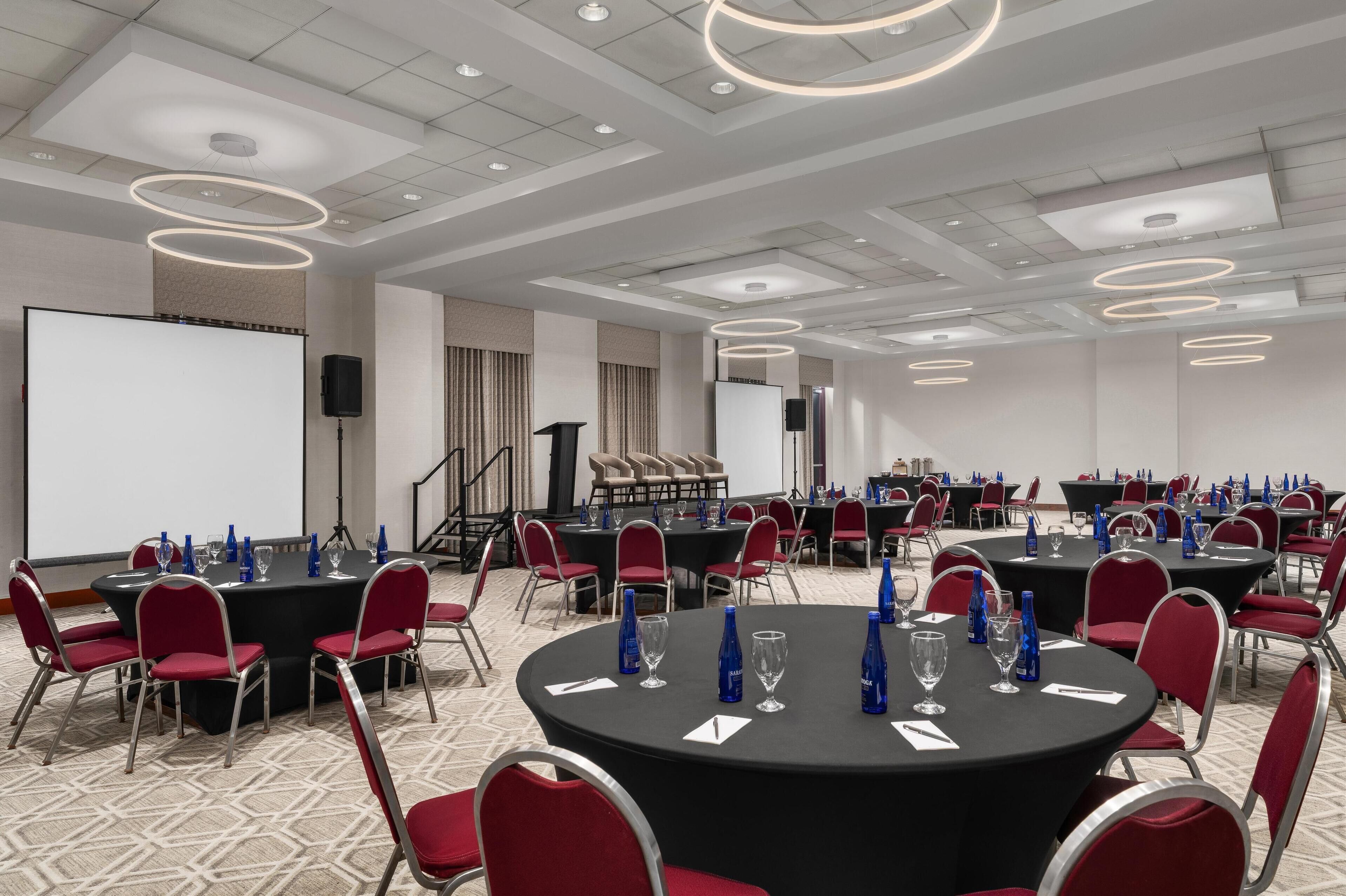Un salón de conferencias con varias mesas, sillas rojas y una pizarra.
