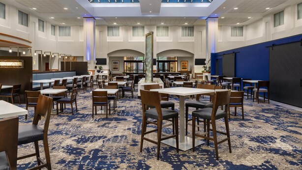 A spacious hotel lobby with a high ceiling, large windows, and a blue carpet. - Embassy Suites Boston Logan Airport (Boston)