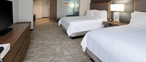 Habitación de hotel con dos camas, un televisor, un escritorio y piso alfombrado.