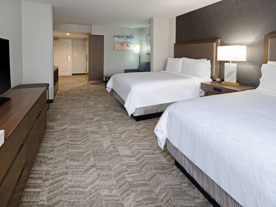 A hotel room with two beds, a TV, a desk, and a carpeted floor.