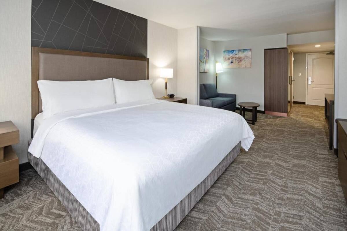 Una habitación de hotel con una cama grande, una mesita de noche, una silla, una pequeña mesa y una puerta.