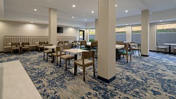 Un comedor amplio con mesas y sillas altas, un largo banco y un gran ventanal con vistas al exterior.