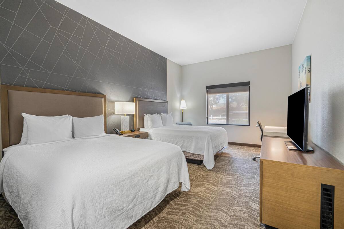 Habitación de hotel con dos camas, televisor de pantalla plana, escritorio y ventana.