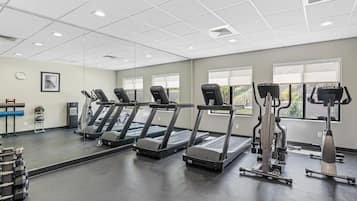 Ein Fitnessstudio mit Laufbändern, Kraftgeräten und einer Spiegelwand.