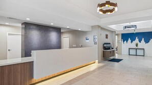 Et moderne receptionsområde med en træreception, en grå accentvæg og en blå væg med et bjergmotiv. Der er en kaffestation og en plante til højre.