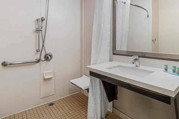 A bathroom with a white sink, a mirror, a shower with a grab bar, and a small bench.