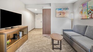 Et moderne hotelværelse med et fladskærms-TV, en sofa, et lille træbord og kunst på væggene.