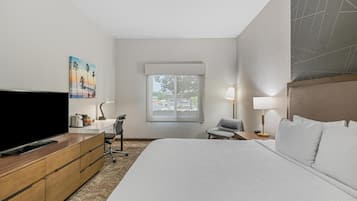 A hotel room with a large bed, a flat-screen TV, a desk with a lamp, a chair, and a window with a view of the outside.