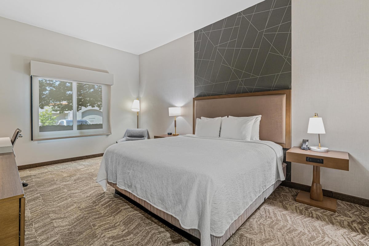 Habitación de hotel con una cama grande, dos lámparas de noche, una mesita de noche, una silla, una ventana con vistas y una pared con un diseño geométrico.