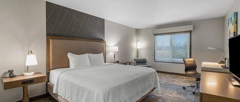 Habitación de hotel con una cama grande, un escritorio, una silla y una ventana.