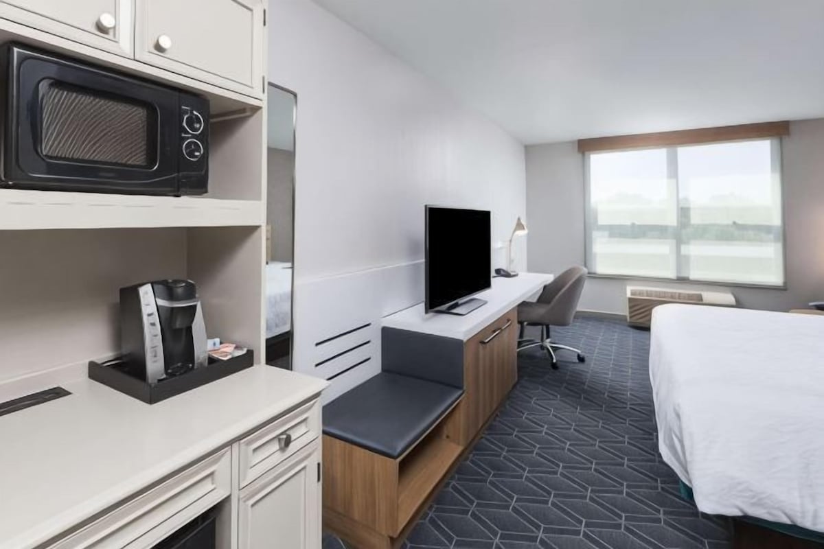 A hotel room with a bed, a desk with a computer, a television, a microwave, and a window with a view.