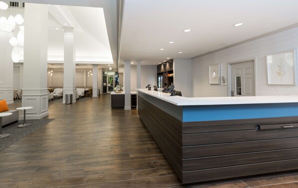 A modern hotel lobby with a reception desk, seating area, and a view of the dining area. - Hilton Garden Inn Oakland / San Leandro (San Leandro)