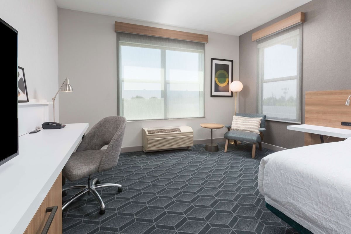 Una habitación de hotel con escritorio, silla, cama y ventanas amplias.