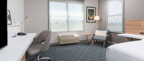 Una habitación de hotel con escritorio, una silla, una cama, una mesita y una ventana.