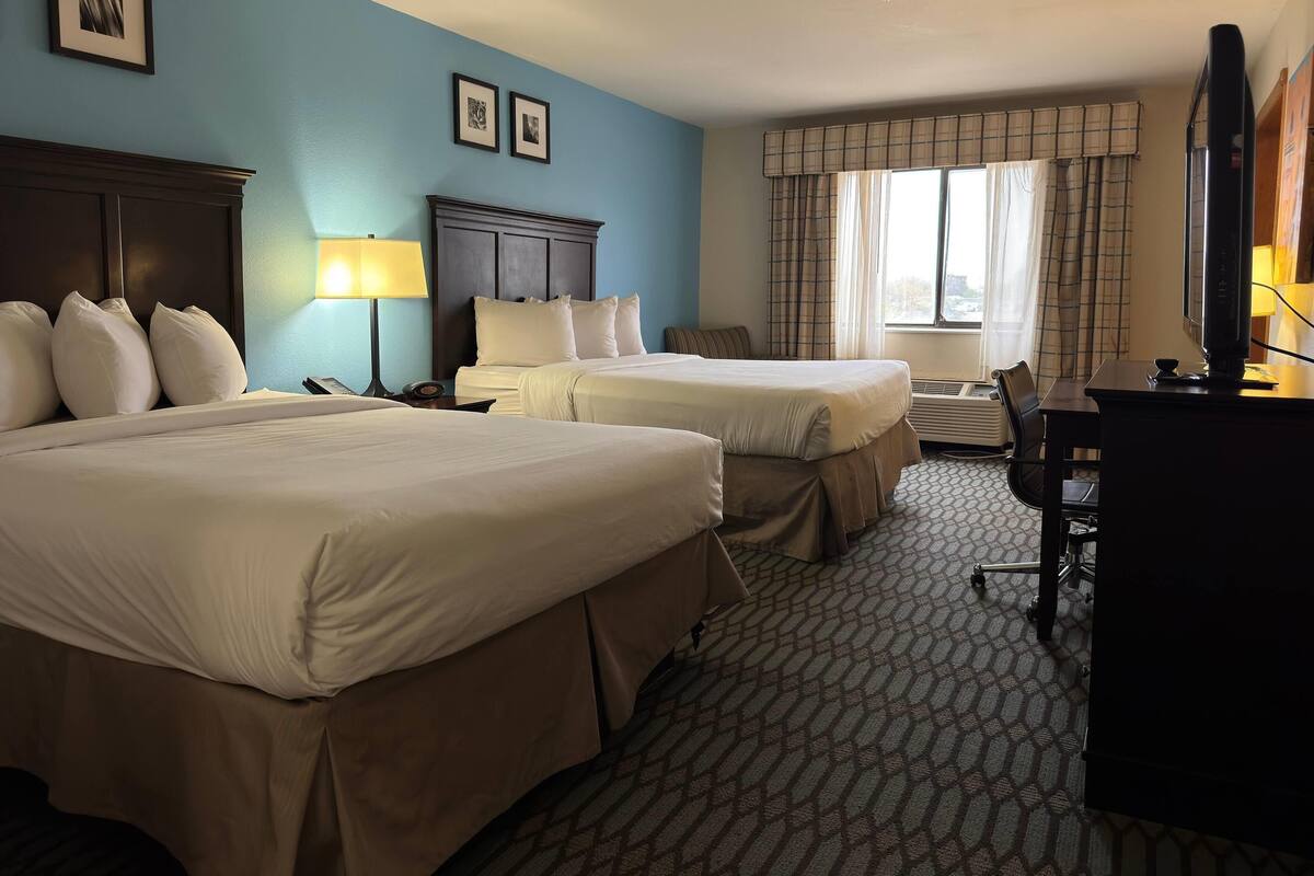Une chambre d’hôtel avec deux lits, un bureau, une chaise, une télévision et une fenêtre avec des rideaux.