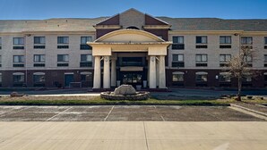 A multi-story building with a central entrance, columns, and a stone fountain in the foreground. - Wingate by Wyndham Lubbock TX South (Lubbock)