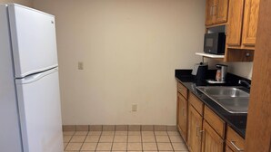 A kitchen with a white refrigerator, wooden cabinets, a black countertop, and a microwave. - Wingate by Wyndham Lubbock TX South (Lubbock)