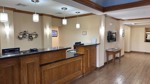 A reception area with a wooden counter, pendant lighting, a wall-mounted TV, and a framed picture. - Wingate by Wyndham Lubbock TX South (Lubbock)