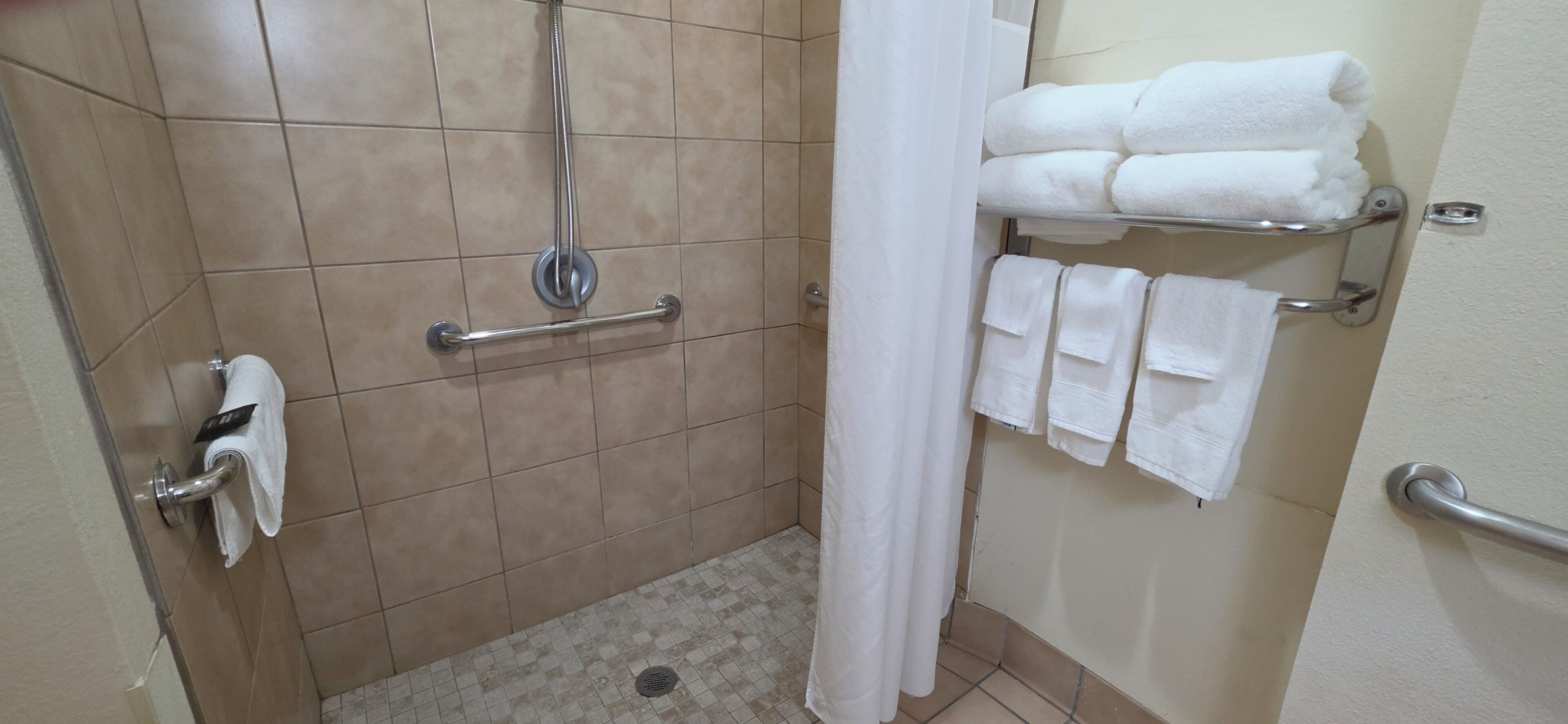 Zona de ducha con barra de apoyo, toallero con toallas dobladas y cortina de ducha.