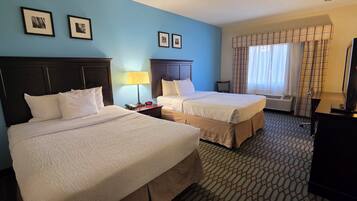 A hotel room with two beds, a TV, a desk, a lamp, and a window with curtains.