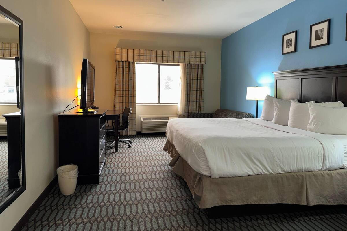 Une chambre d’hôtel avec un lit, un bureau, une chaise et une fenêtre avec des rideaux.