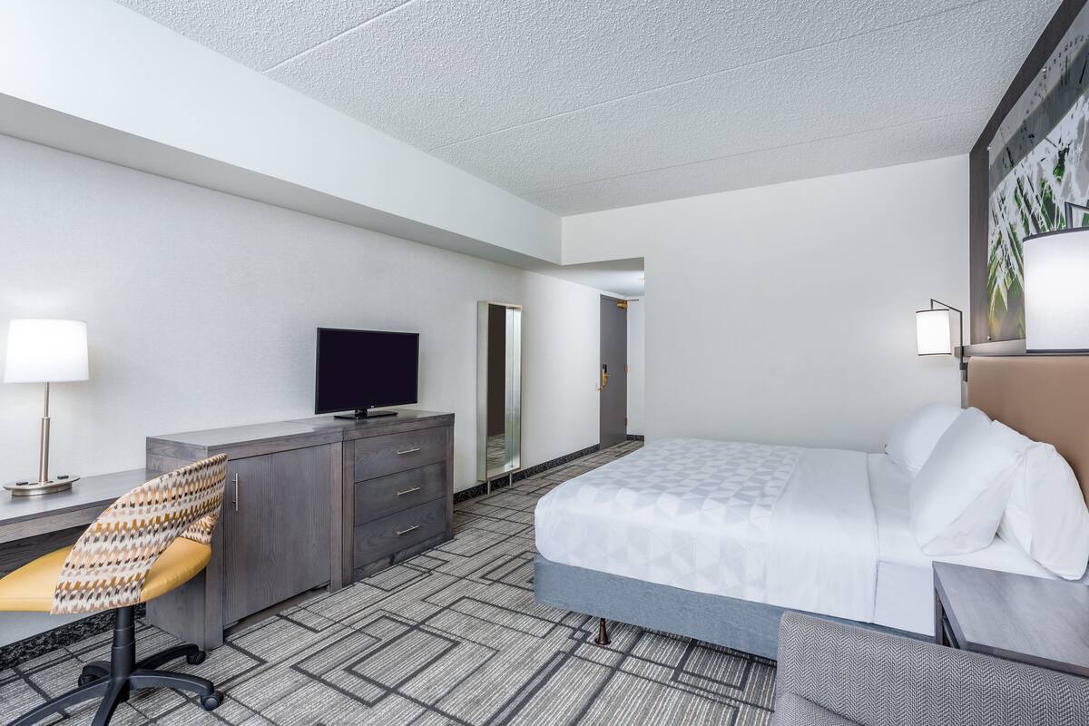 A hotel room with a bed, a desk with a chair, a television, and a wardrobe.