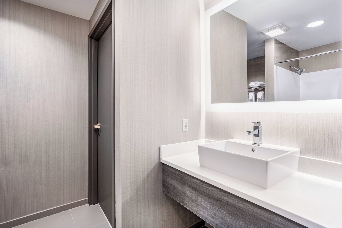 A modern bathroom with a white sink, a large mirror, and a shower area.