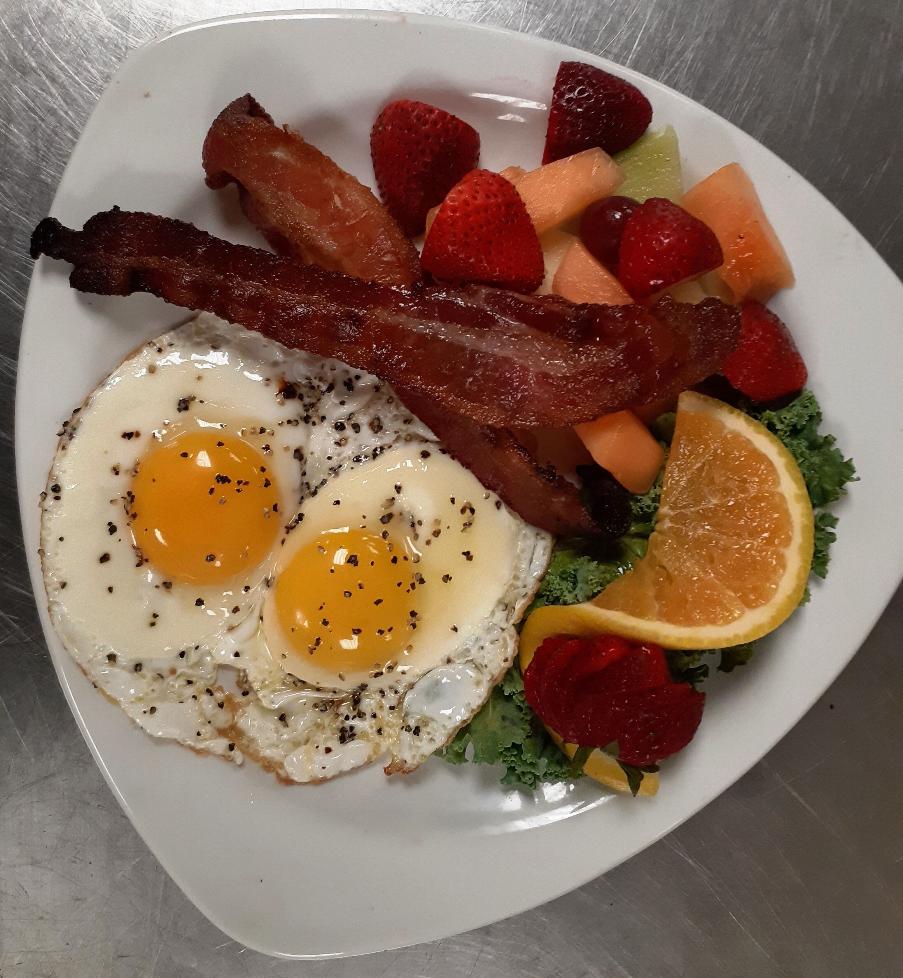 Une assiette contenant des œufs, du bacon, des fraises, du melon et de la laitue.