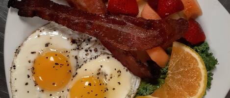 Une assiette contenant des œufs, du bacon, des fraises, du melon et de la laitue.