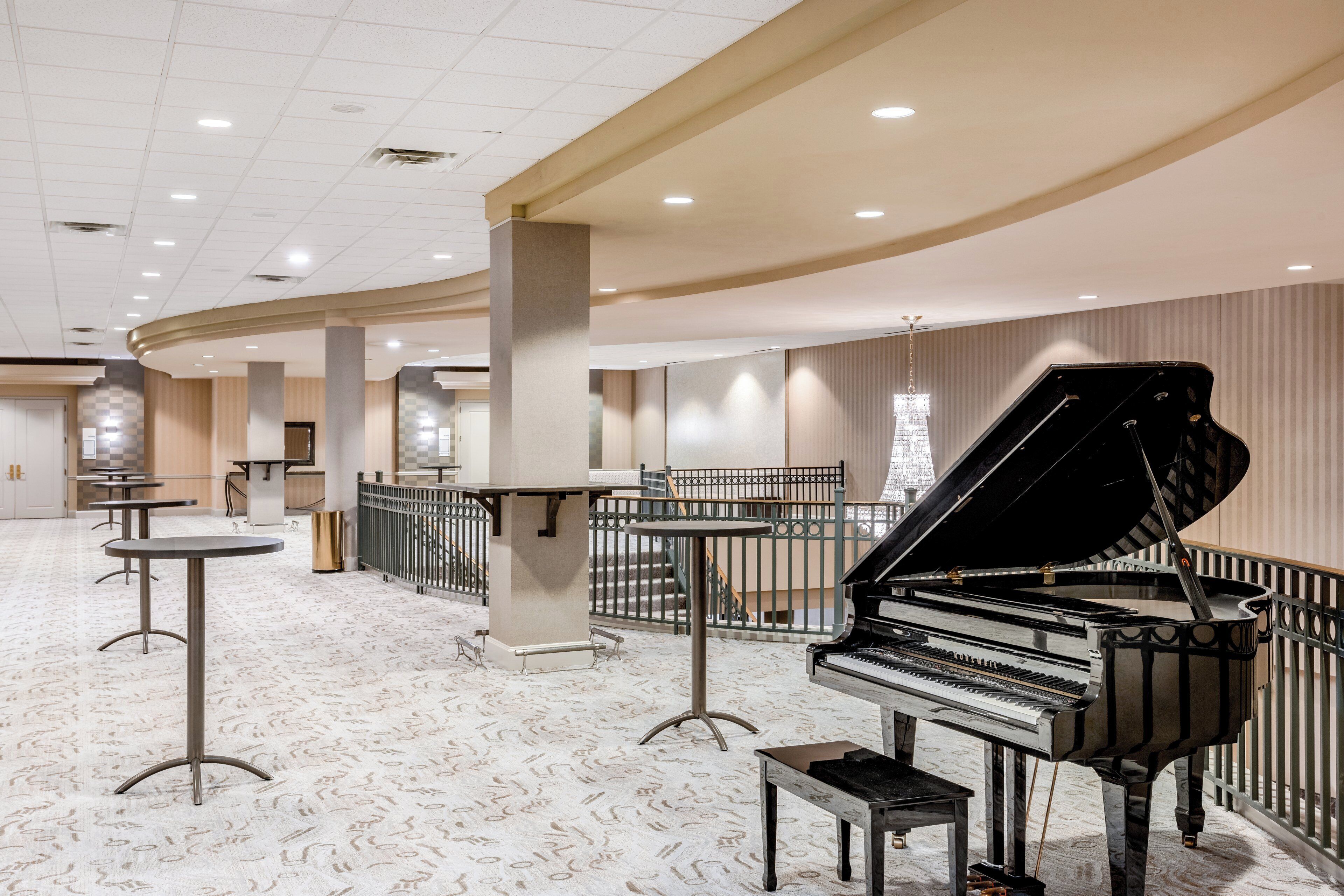 A spacious hotel lobby with a grand piano, seating areas, and a high ceiling with recessed lighting.
