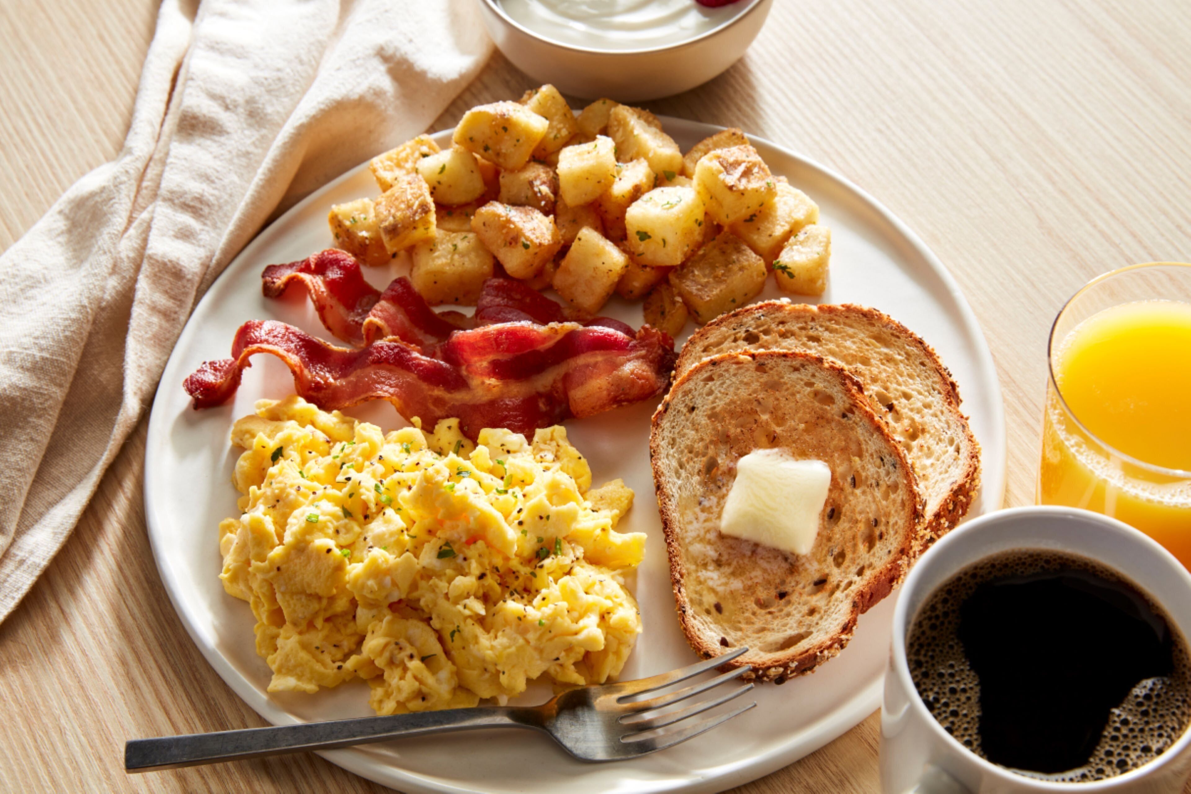 A plate with scrambled eggs, bacon, roasted potatoes, toast with butter, and a glass of orange juice.