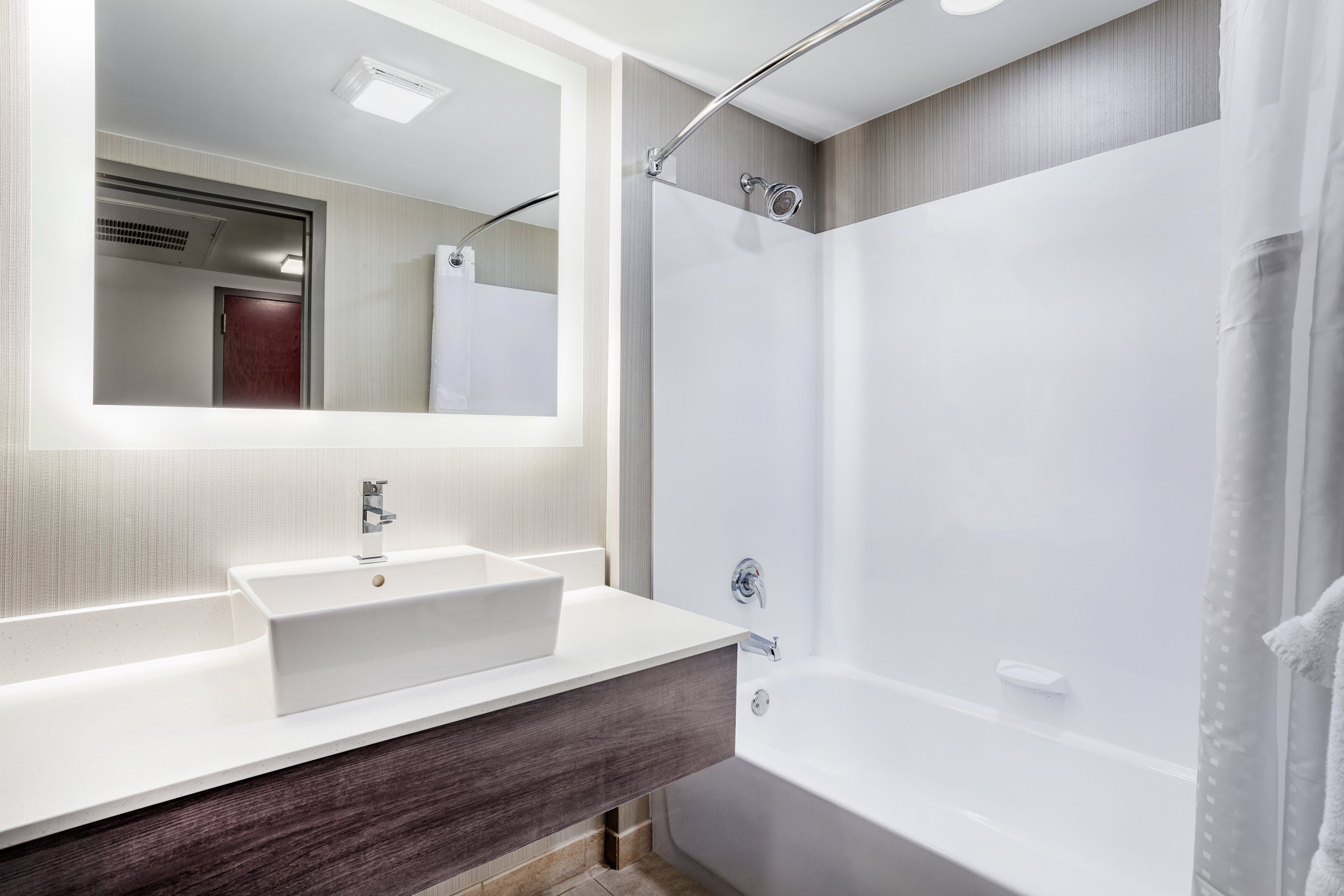 Un baño moderno con un espejo grande, un lavamanos blanco, una bañera y una zona de ducha.