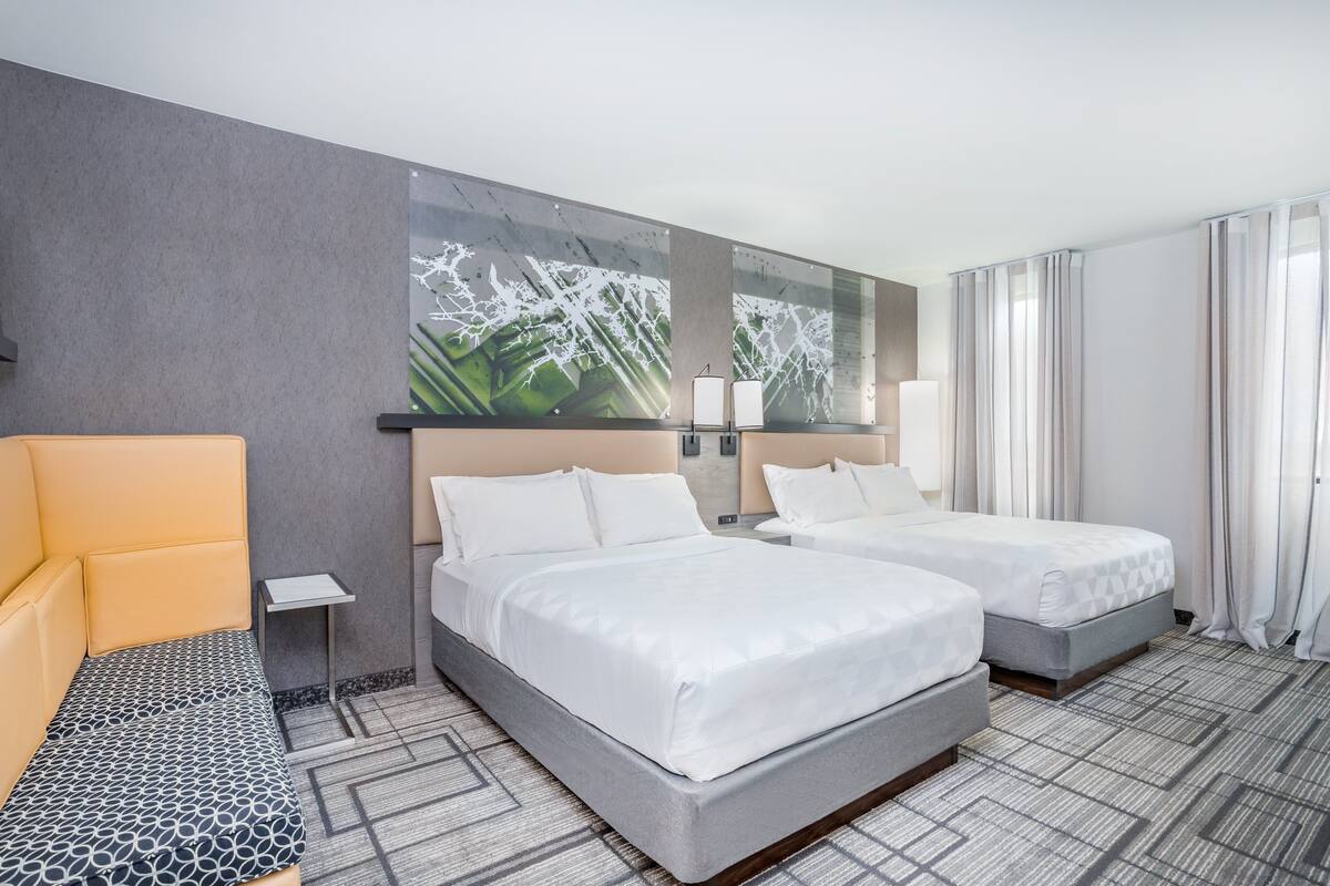 A hotel room with two beds, a sofa, a small table, and a large abstract painting on the wall.