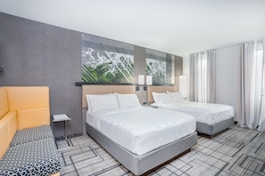 A hotel room with two beds, a sofa, a small table, and a large abstract painting on the wall. - Holiday Inn Lafayette-City Centre by IHG (Lafayette)